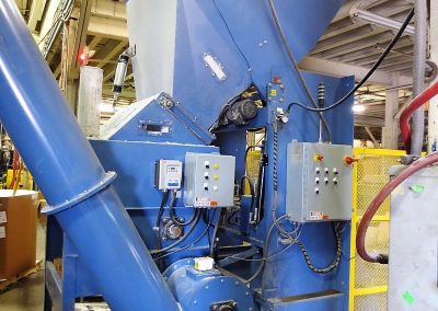 Dumper unloading flake material into a high capacity live bottom bin with a screw conveyor connected for transfer to downstream equipment.